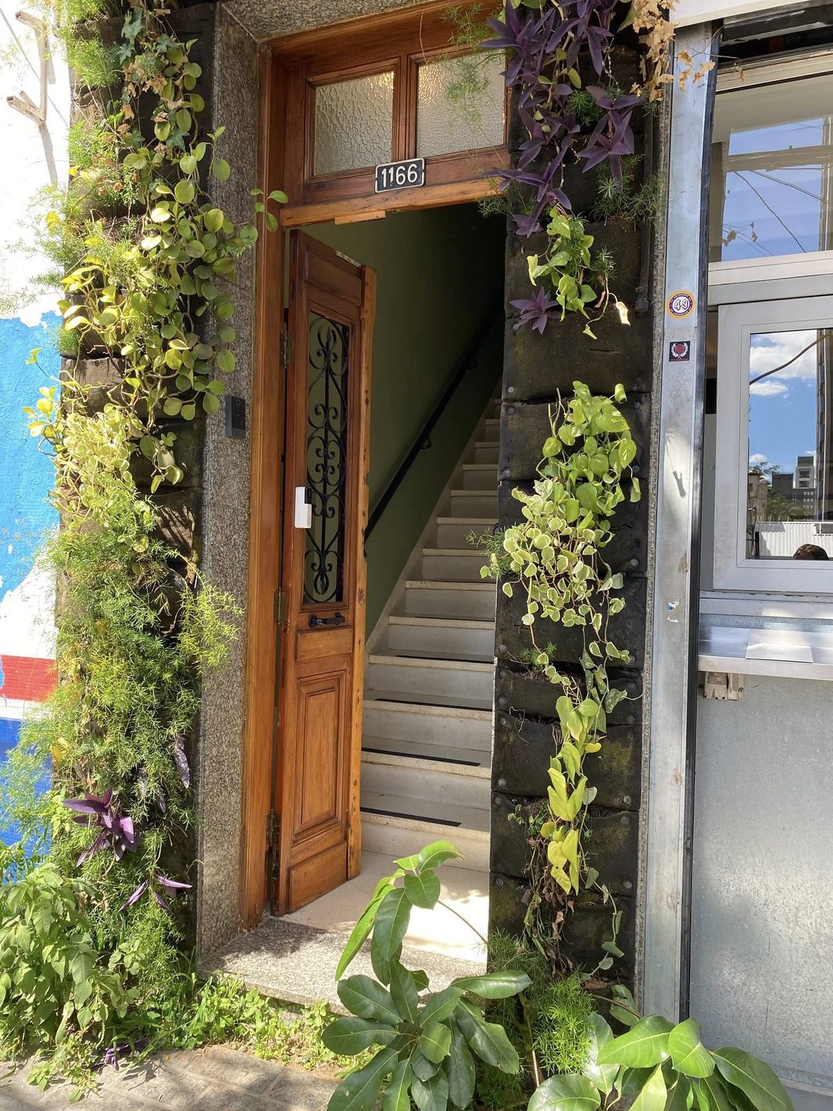 Entrada do prédio da clínica, com porta de madeira e plantas